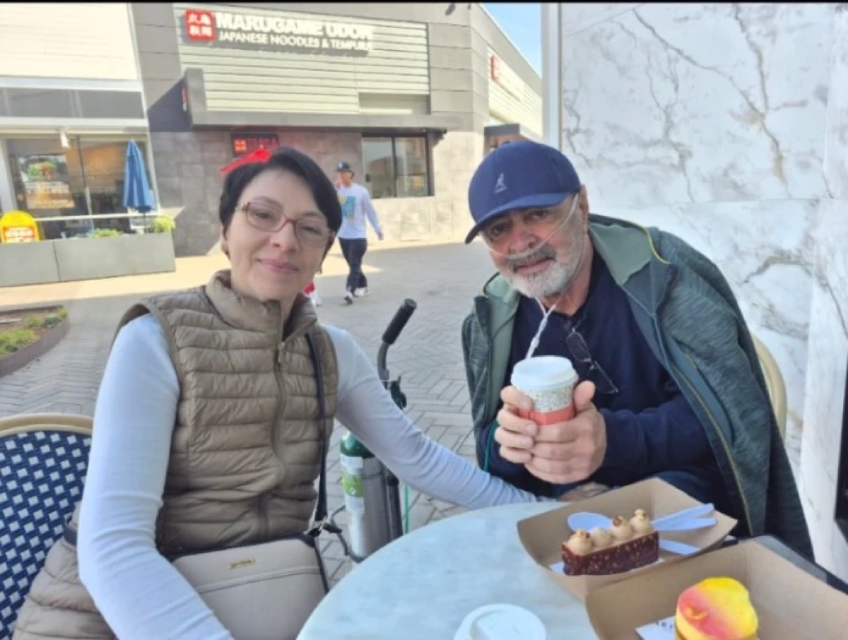 Yossi and his wife at a café, the oxygen concentrator beside him
