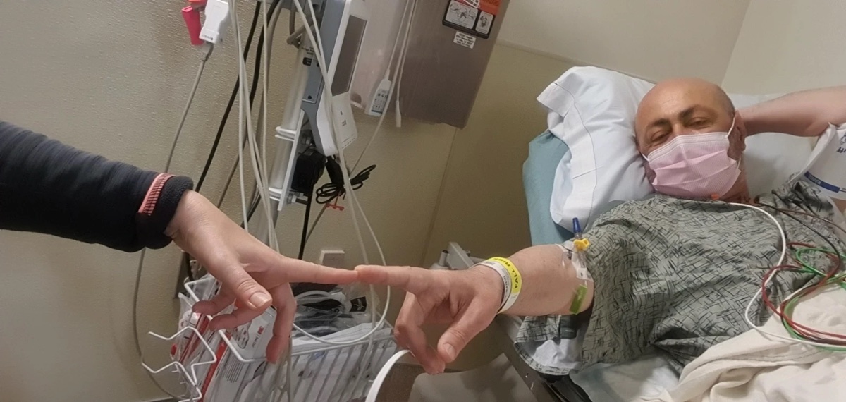 Yossi in a hospital bed, holding his wife's hand