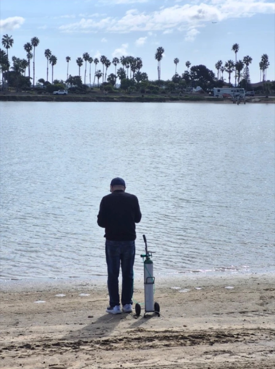 Yossi on the beach with a portable oxygen tank, looking out at the water